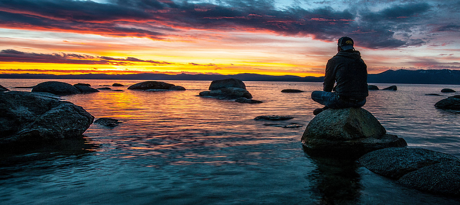 A person sitting on a rock overlooking a serene lake at sunset.