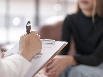 A healthcare professional is conducting a medical consultation with a patient, using a clipboard to document information.